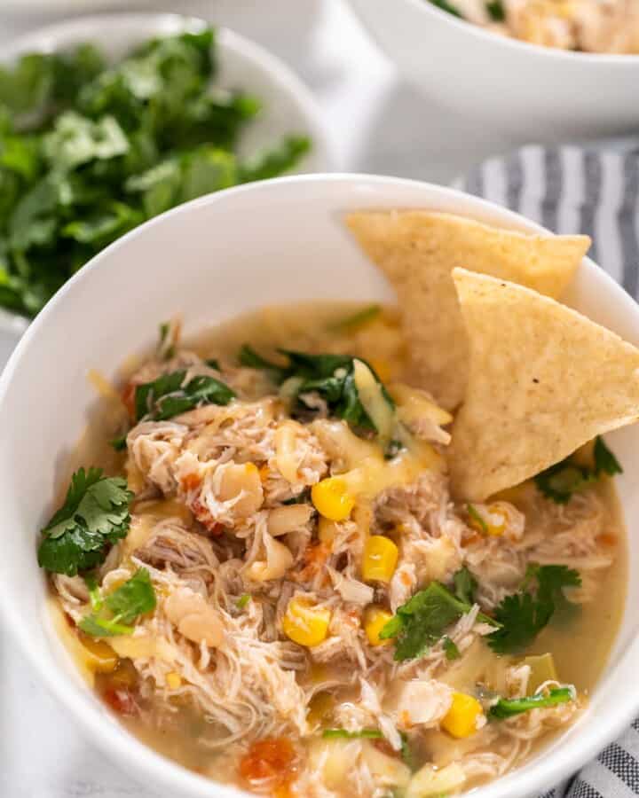 Close up of instant pot white bean chicken chili with two tortilla chips dipped in the soup of a white bowl.