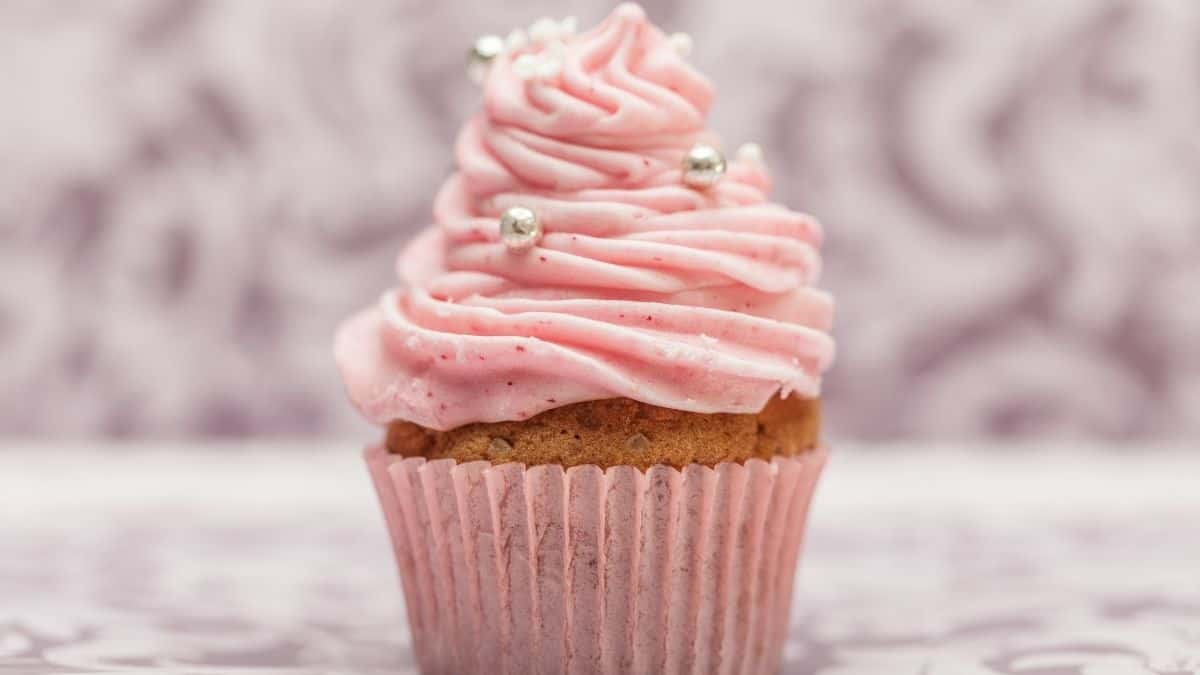 a pink frosted cupcake in a pink cupcake wrapper on a pink background; silver sprinkles dot the frost - an example of a carb.