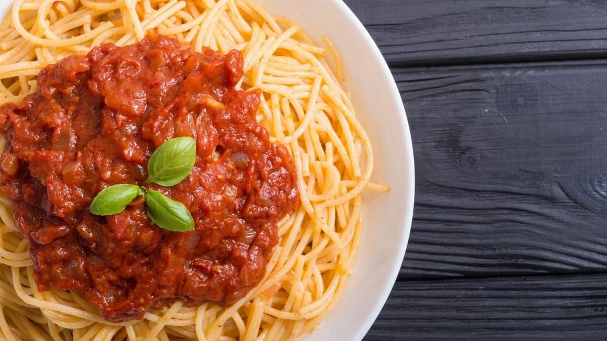 a shallow white bowl filled with spaghetti noodles and red sauce on a black table, this meal is a great example of carbohydrates.