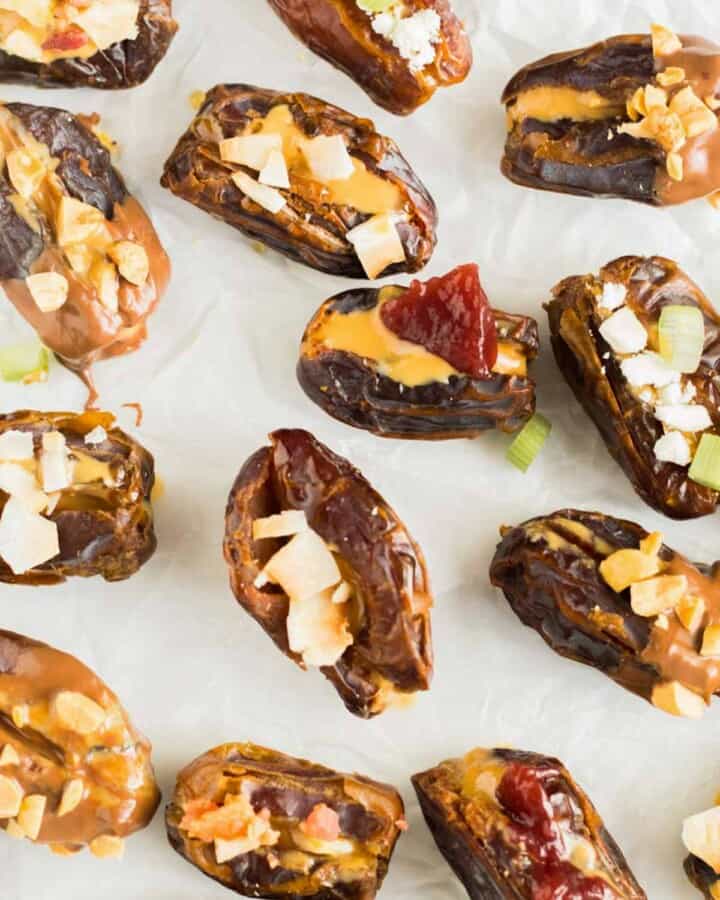 different variations of stuffed dates on white surface with jelly, nuts, peanut butter, goat cheese, coconut
