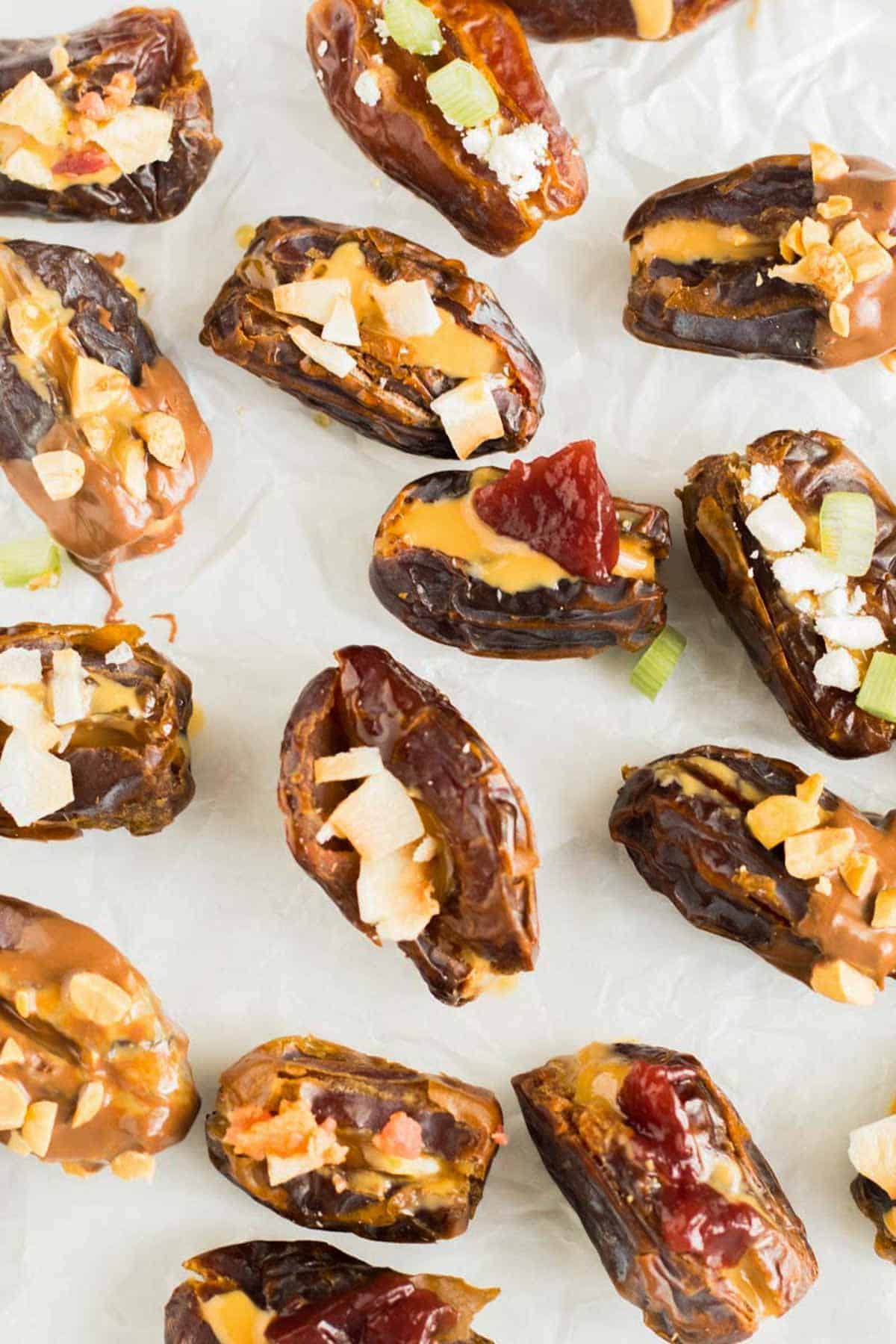 different variations of stuffed dates on white surface with jelly, nuts, peanut butter, goat cheese, coconut