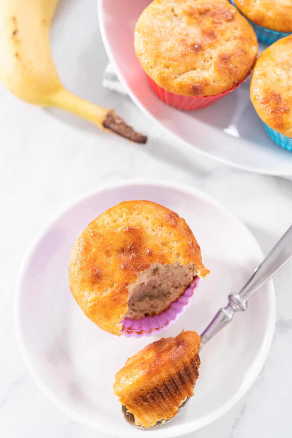 A spoonful of banana protein muffin next to the muffin in a purple cupcake holder.