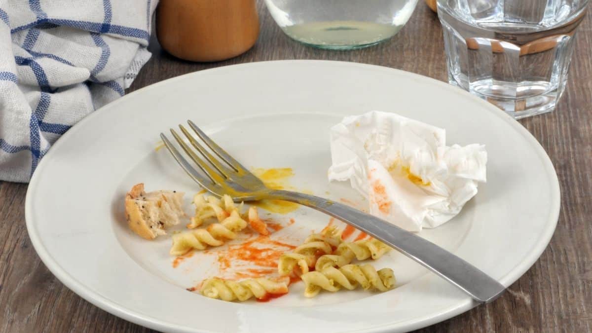a dirty plate after a finished meal with a fork on top of plate, water glass and empty glass next to it.
