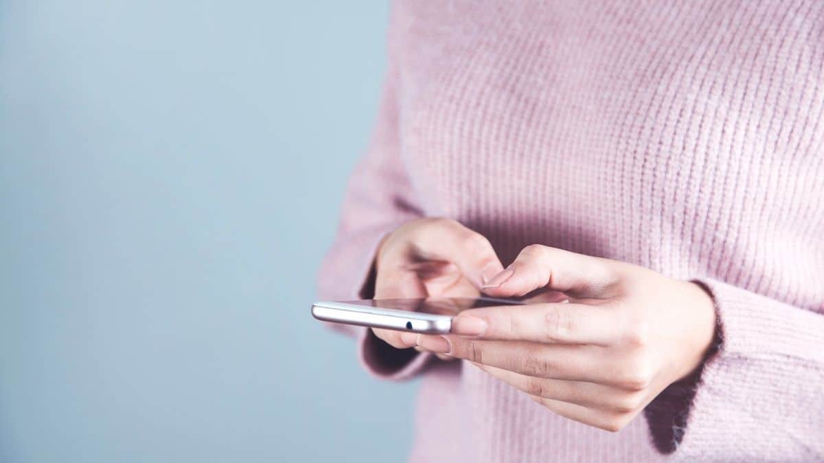 a woman in pink sweater holding a phone ready to call a friend.