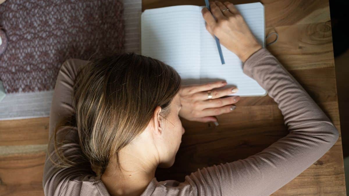 sleeping woman at a table leaned over a notebook.