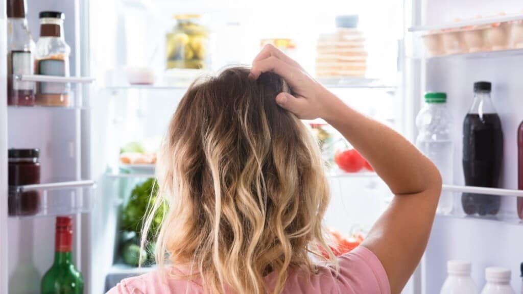 woman standing at open refrigerator scratching her head.