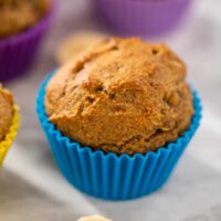A Almond Flour Banana Muffin in a blue muffin liner with sliced bananas on grey counter.