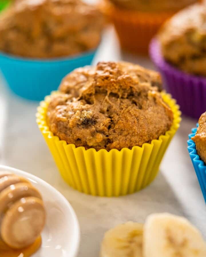 A Almond Flour Banana Muffin in a yellow muffin line with colorful muffins in the background.