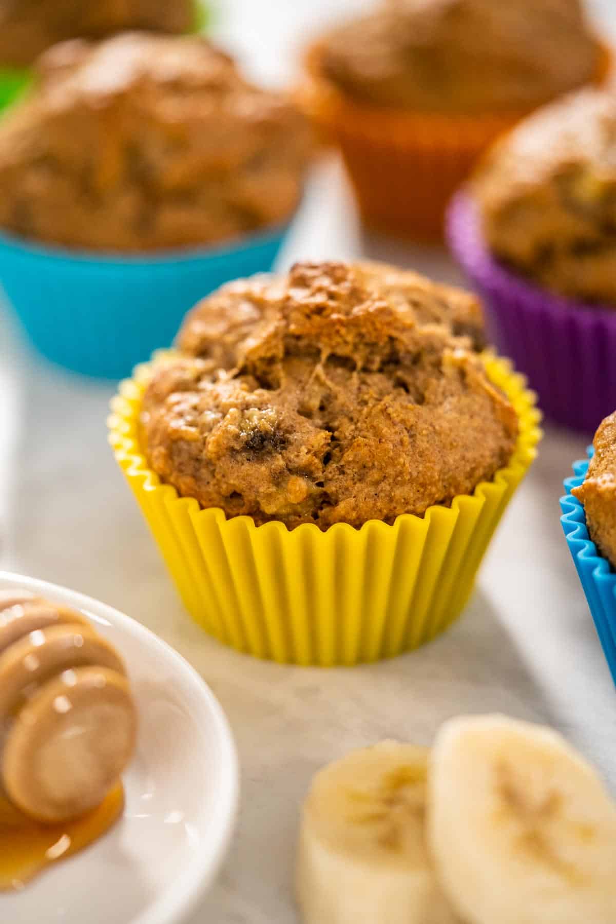 A Almond Flour Banana Muffin in a yellow muffin line with colorful muffins in the background.