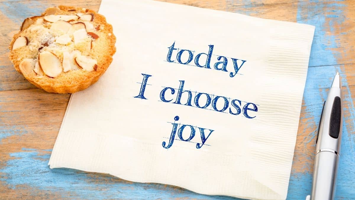 a napkin that reads _today I choose joy_ next to an almond tart on a wooden table with destressed blue paint.
