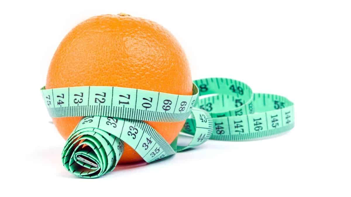 a whole orange wrapped in a green tape measure on a white background.