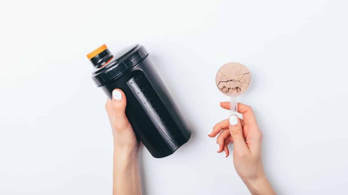 a woman holding a protein shake cup and scoop or protein powder.