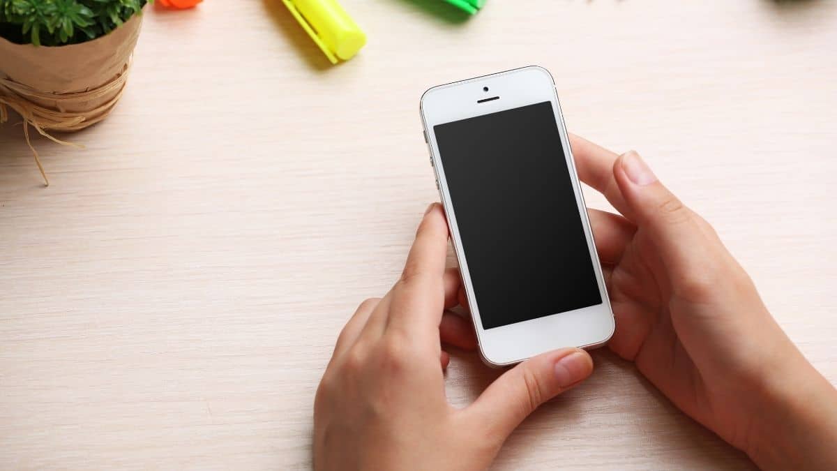 a woman holding a white iphone against a desk background.