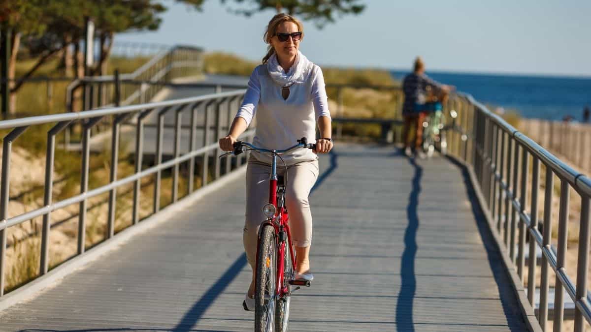 a woman in a white sweater joyfully riding her bike on a beach boardwalk.