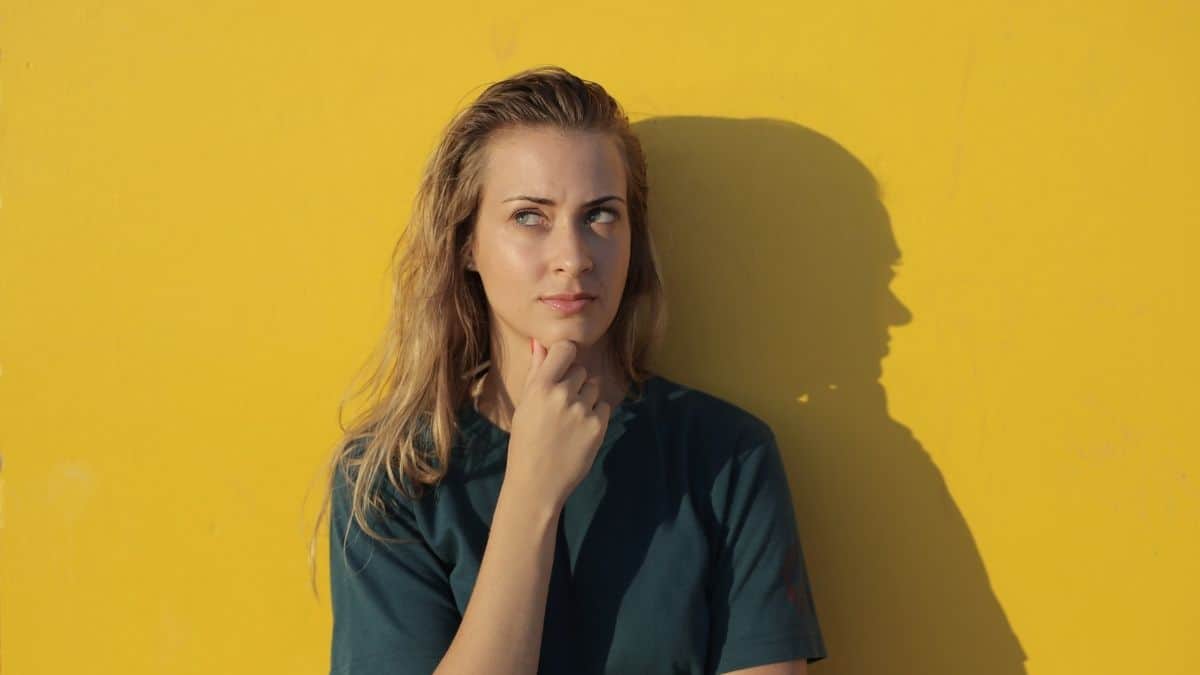 a woman wearing a forest green shirt contemplating something, holding her hand up to her chin.