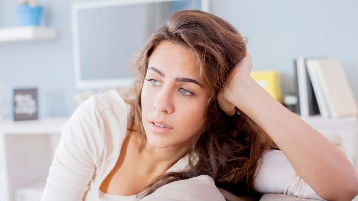 a woman with long brown hair sitting on a couch with her head resting on her hand.