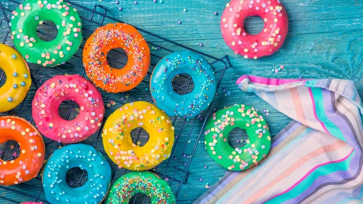 brightly colored donuts on a cooling rack with a striped towel laying on a blue wooden table.