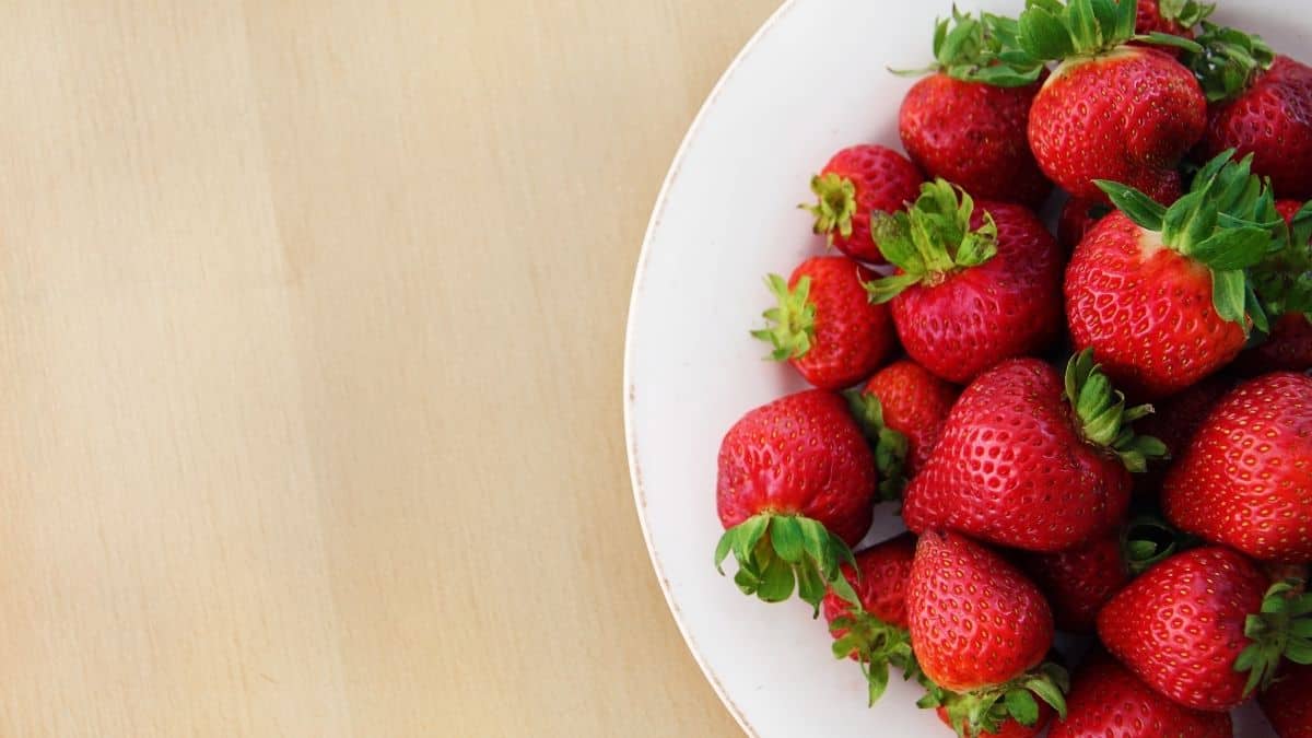fresh strawberries on a white plate on a wooden table.