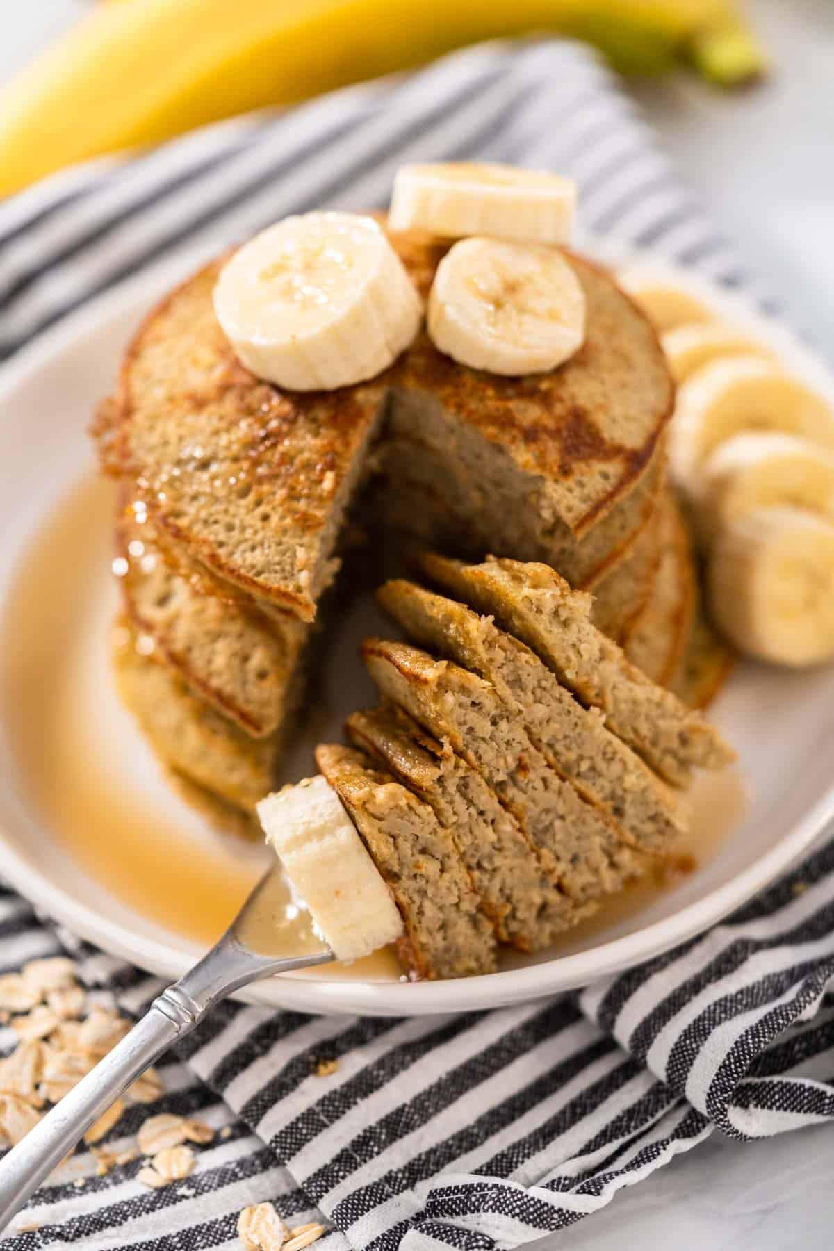 Maple syrup and bananas topping a stack of three ingredient banana oat pancakes.