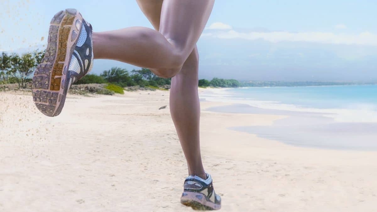 a close up shot of a woman's running shoes mid-stride as she runs on a sandy beach, this could be intuitive exercise for her.