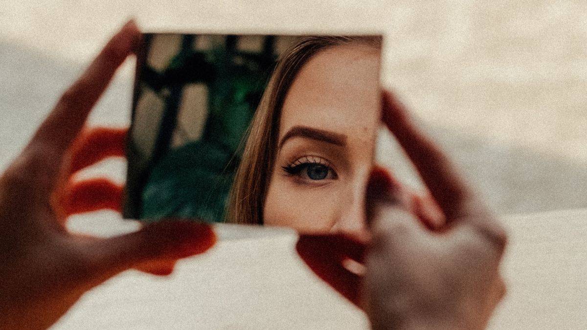 a woman's face is reflected in a small rectangular mirror.