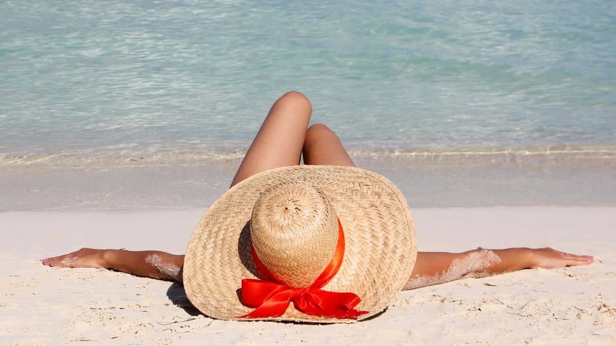 woman lying on the beach with a straw hat and red ribbon.