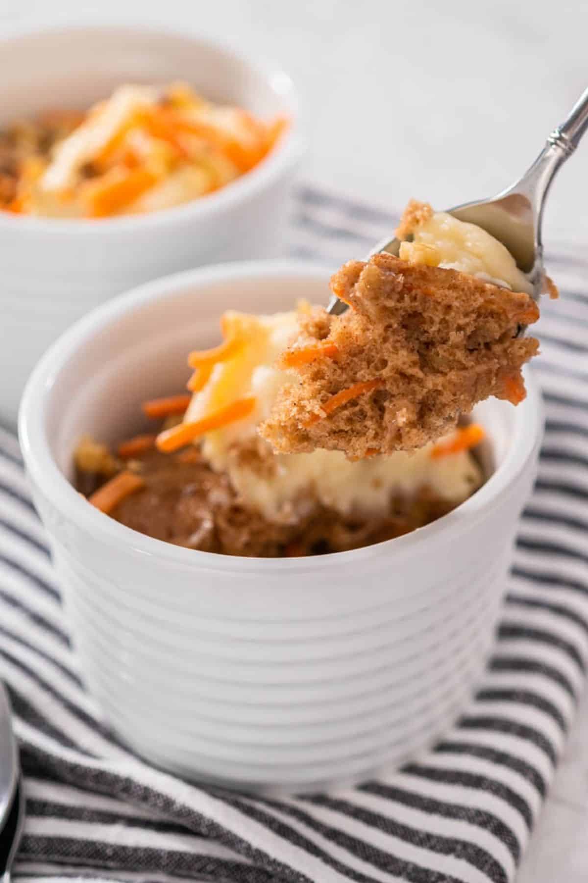 A small mug/ramekin with a personal carrot cake, a spoon removing a portion.