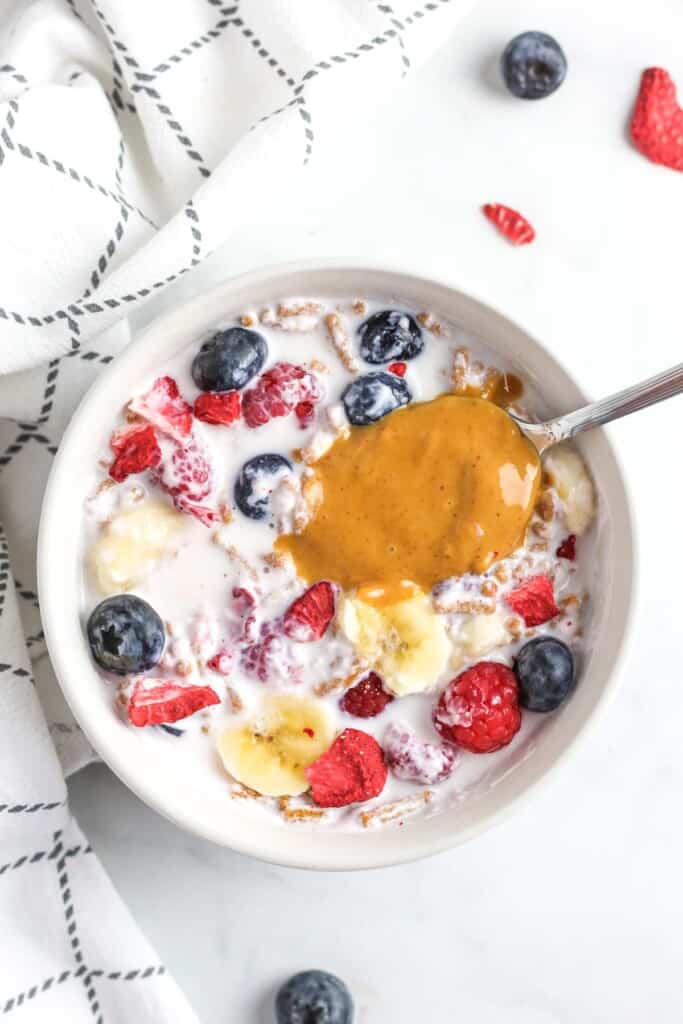 A close up of a bowl of yogurt, fruit, and a large spoonful of peanut butter.