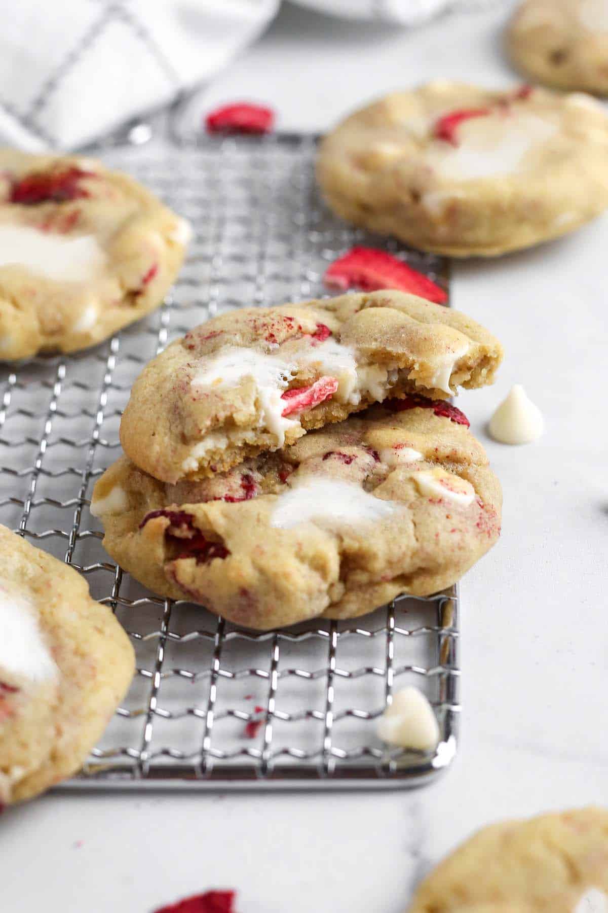 Strawberry cheesecake cookies on a cooking rack, two stacked on top of each other, one with a bite out.