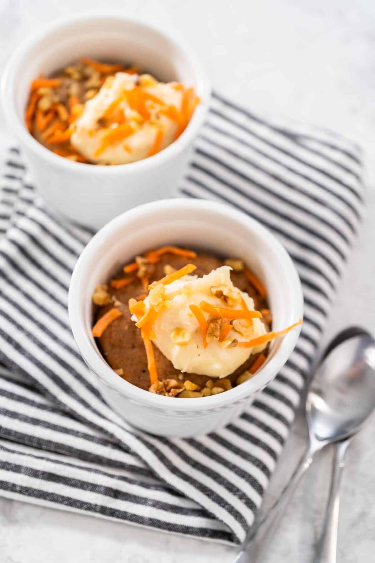 Two mugs of a carrot mug cake on a navy striped napkin.