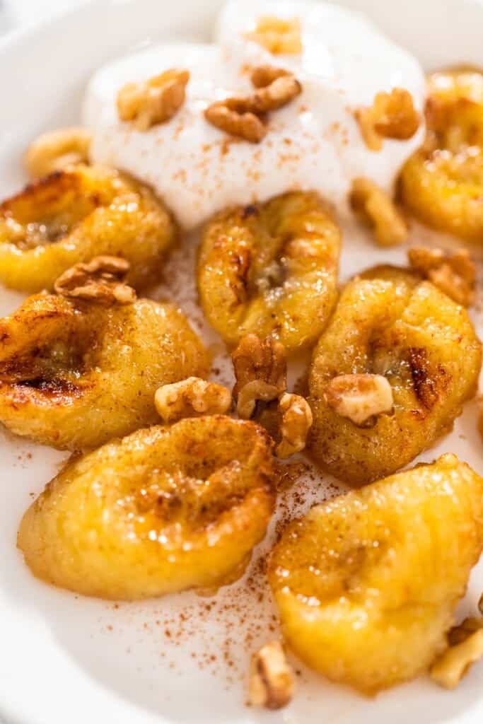 A close up of air fryer sliced bananas, topped with whipped cream.