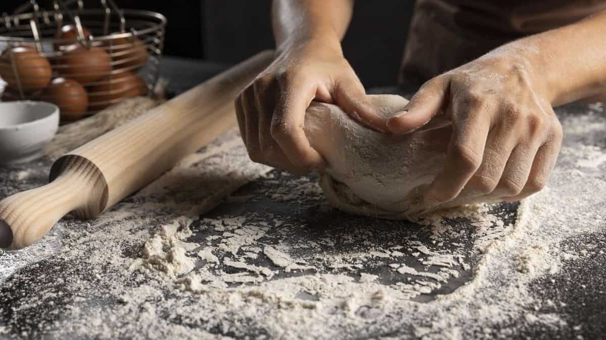 hands kneading dough on a table with flour.