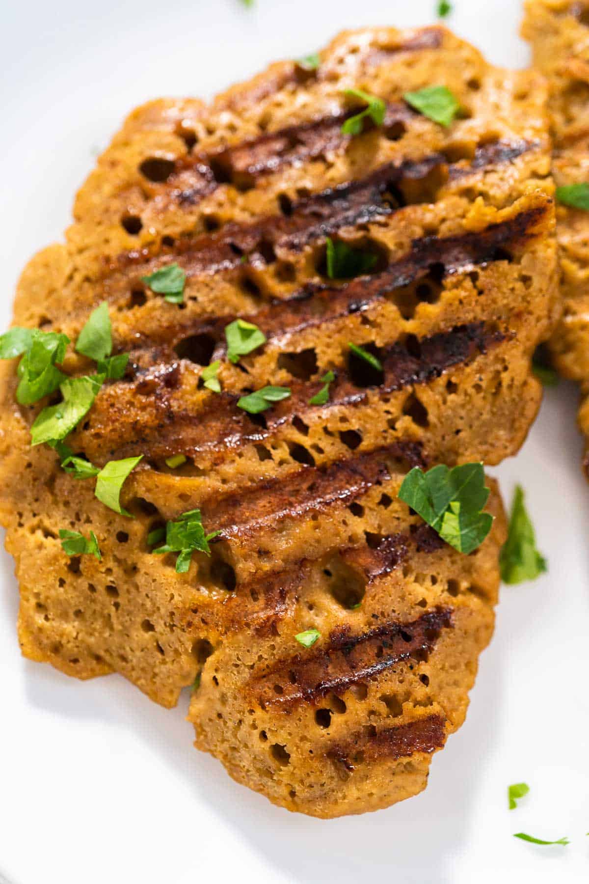 A single seitan chicken cutlet, with grill marks and sprinkled with fresh parsley.