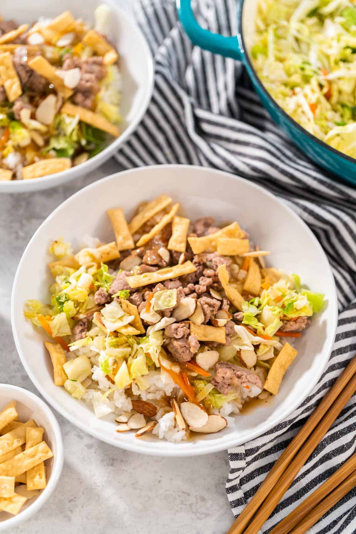 Two bowls of warm asian salad stir fry, topped with fried wontons and ground turkey.