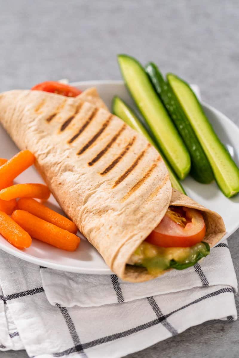 A tuna melt wrap on a plate, served with vegetables on the side.
