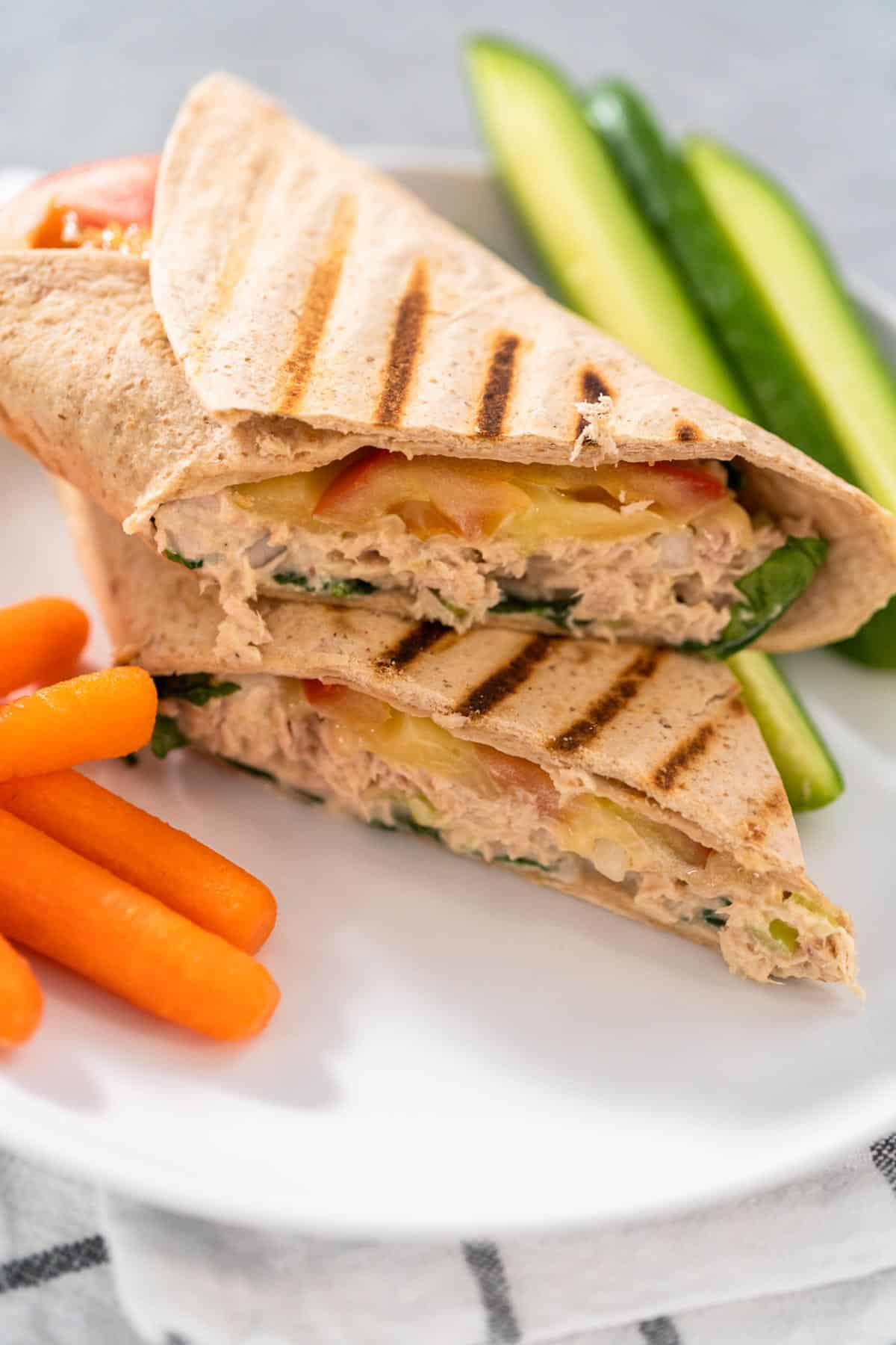 A tuna melt wrap with cheese on a plate with vegetables on the side.