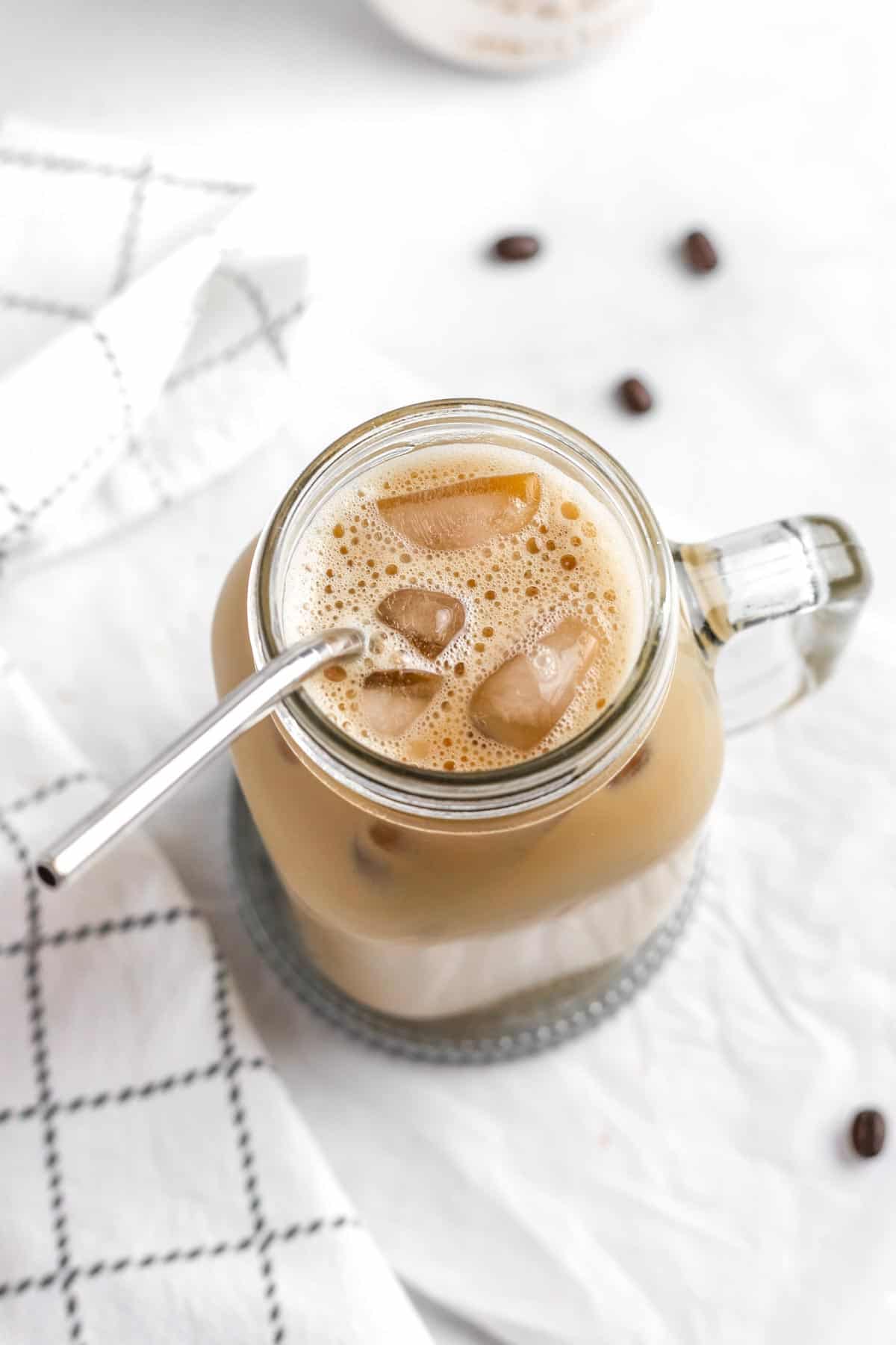 An overhead view of iced coffee in a glass with a stainless steel straw.