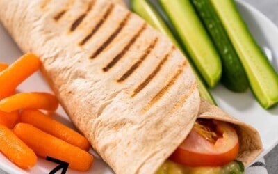 A plate with a tuna melt wrap with grill marks, served with veggies.