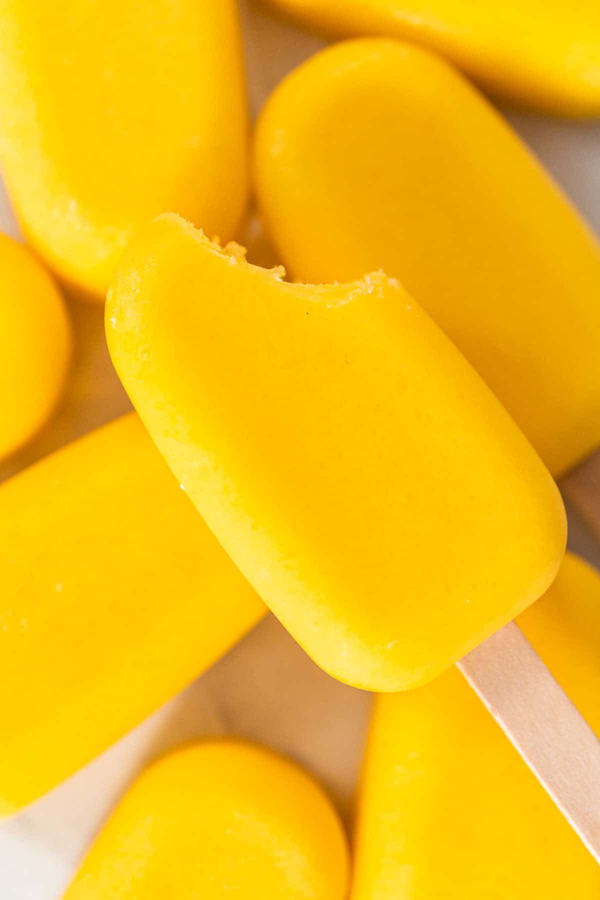 homemade popsicles on a white counter, stacked with a bite taken out of one.