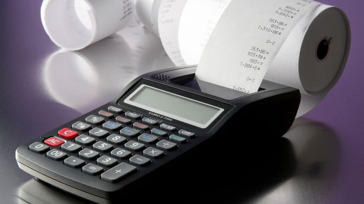 a black calculator with a trailing roll of white paper sitting on a purple background.