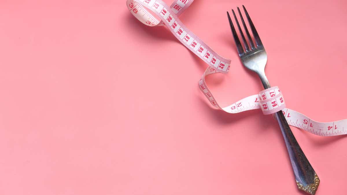 a fork with a measuring take wrapped around the handle on a pink background.