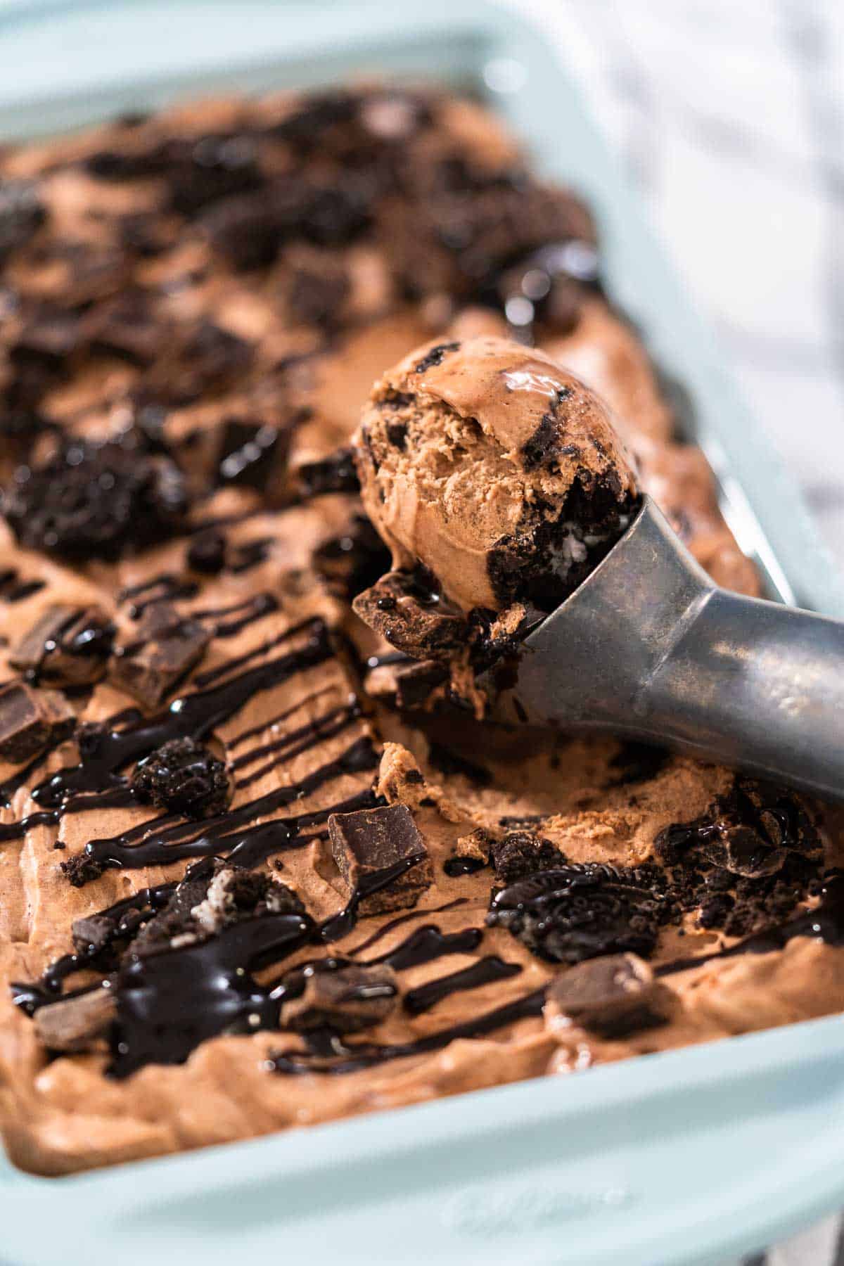 A close up of a pan of ice cream with a scoop taking out chocolate.