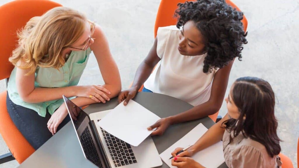 Three women sitting around a paper and computer