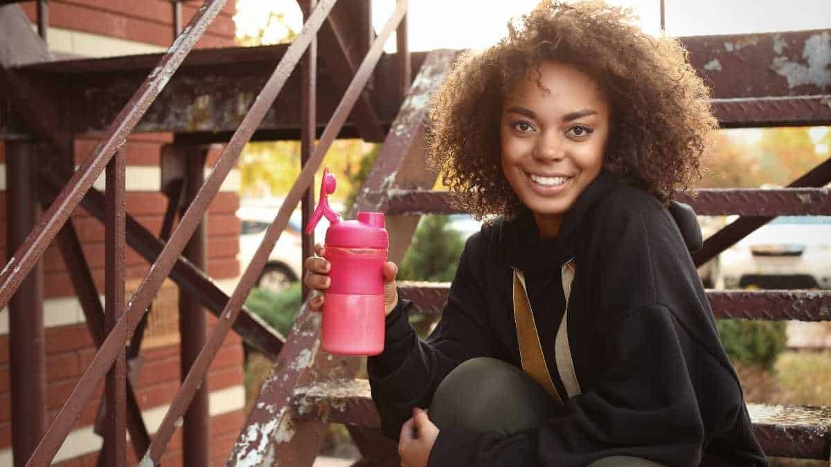 a woman holding a pink bottle with protein drink.