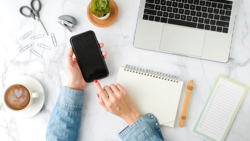 woman holding phone with computer and notebook