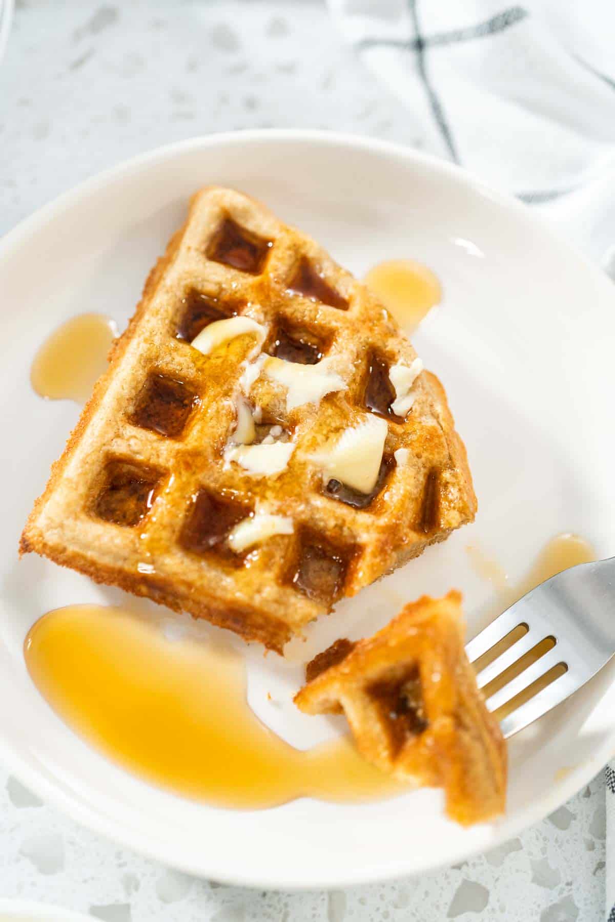 A small oat flour waffle with butter, drizzled with syrup.