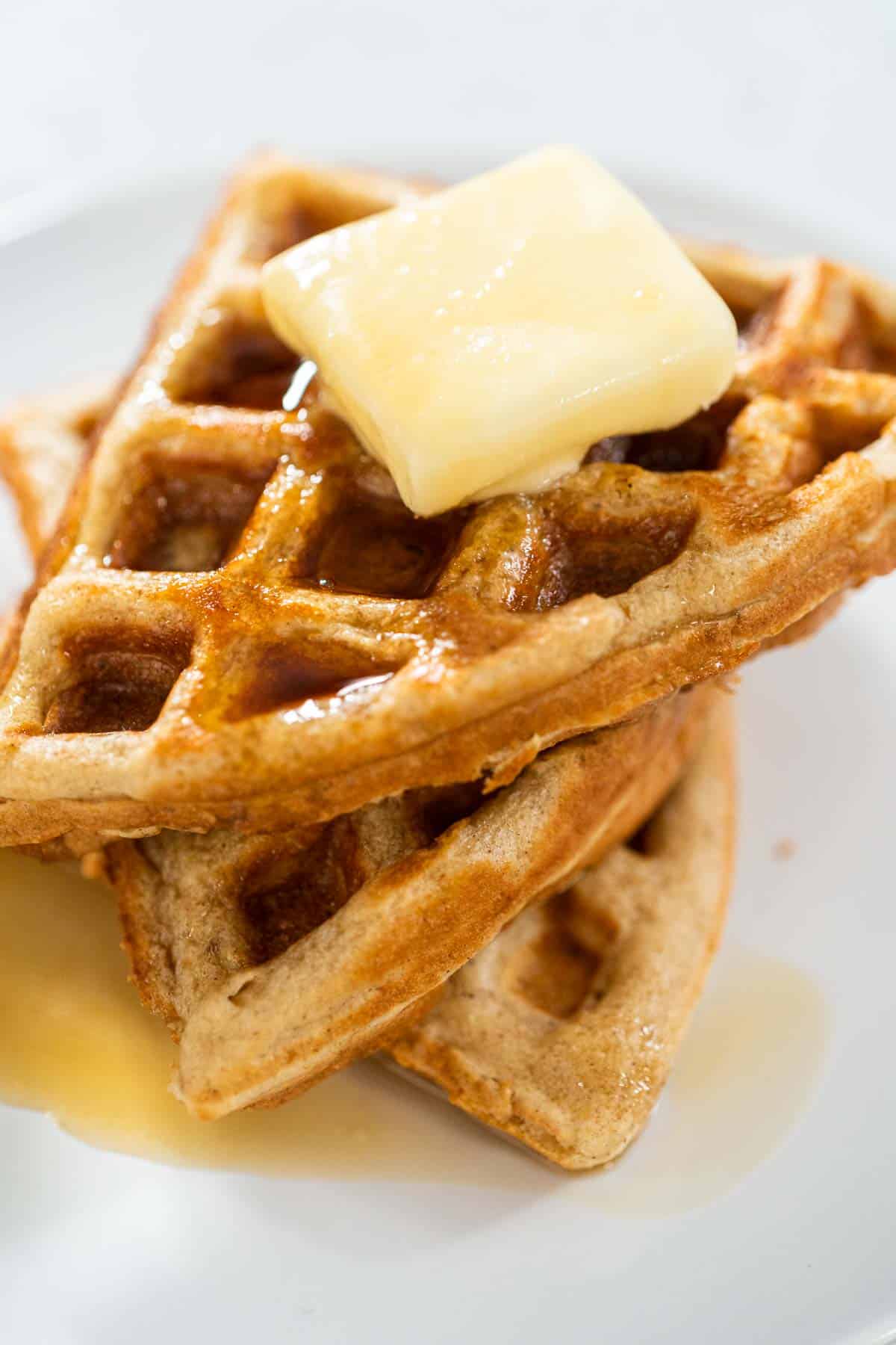 A stack of three Oat Flour Waffles with a pat of butter on top and syrup on plate.