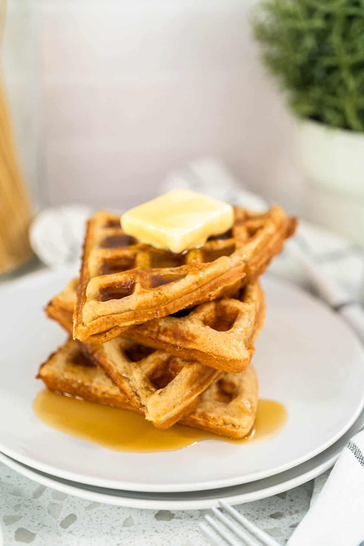 Stack of four Oat Flour Waffles with a pat of butter and syrup on top.