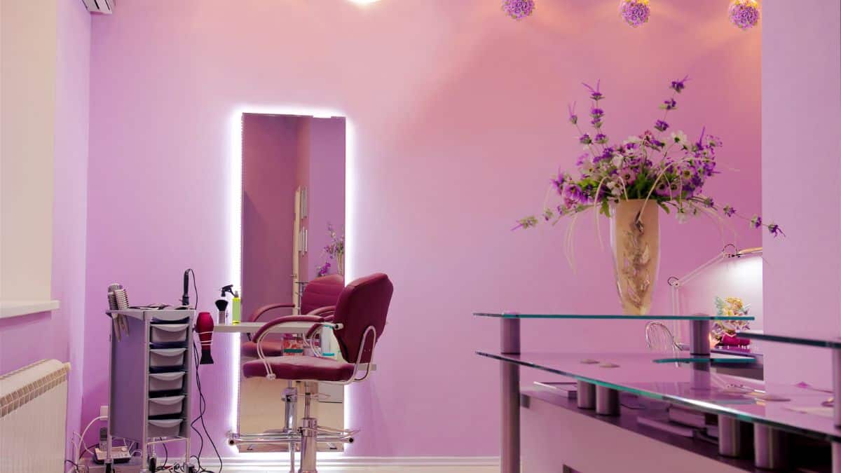a hair salon with pink walls, flowers and chair in front of a full length mirror.