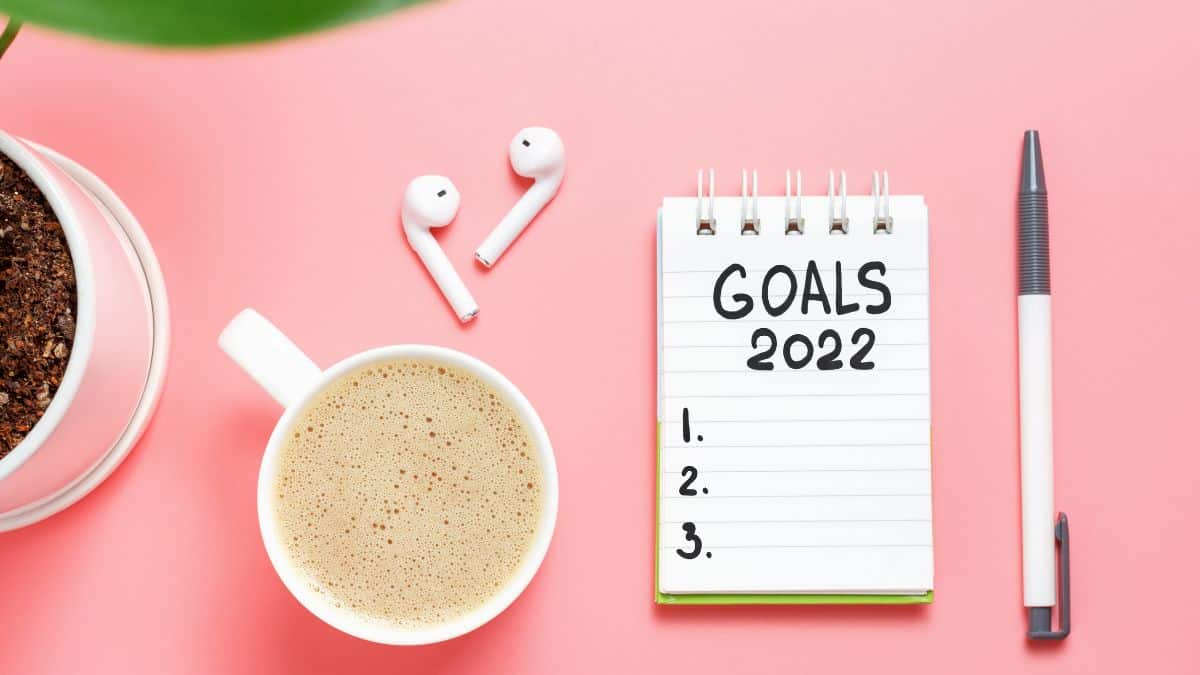 a notepad with goals 2022 written on it with a cup of coffee, pen and airpods nearby.